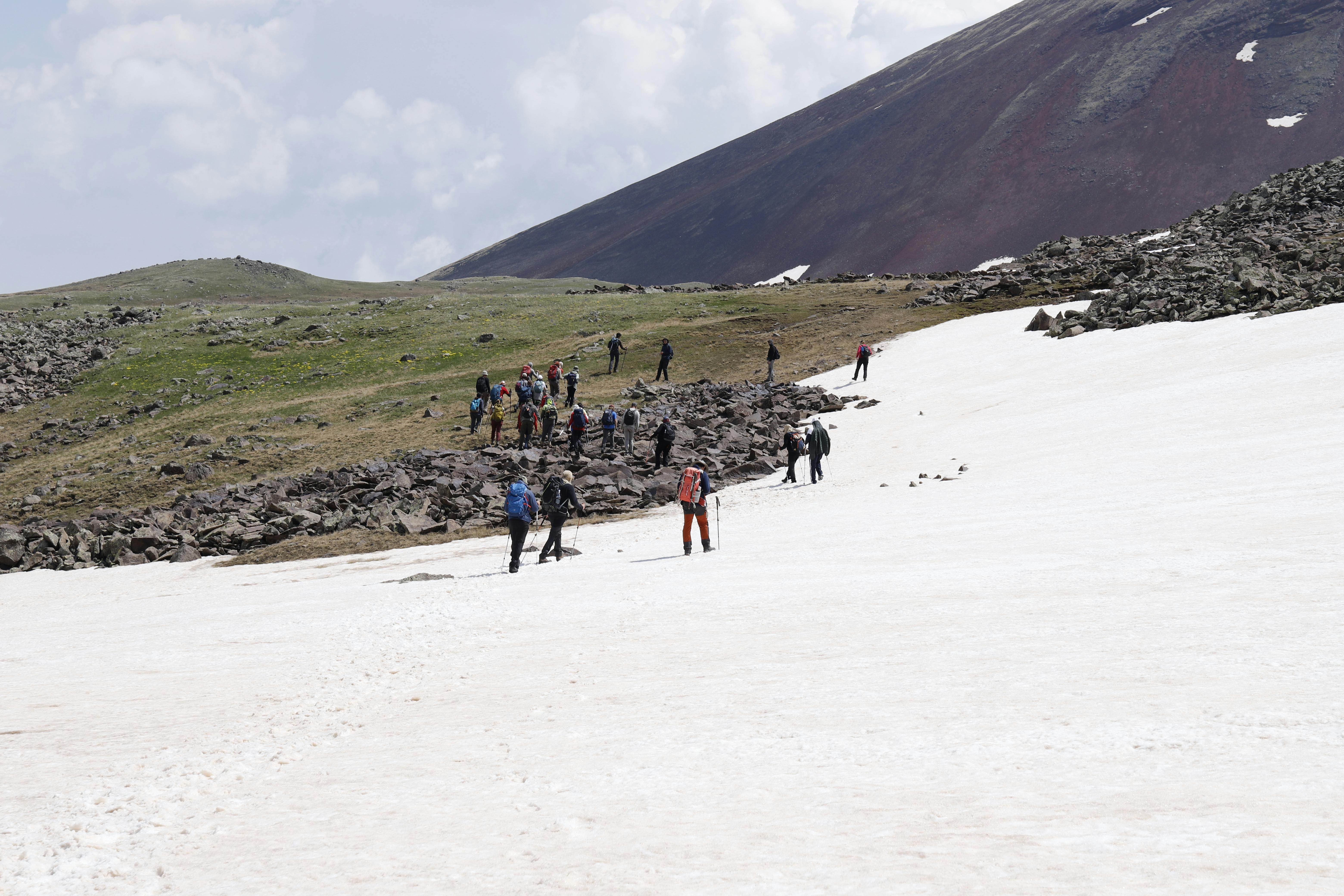 Hikers trek up a snow-covered mountain trail against a scenic backdrop, showcasing adventure and nature.